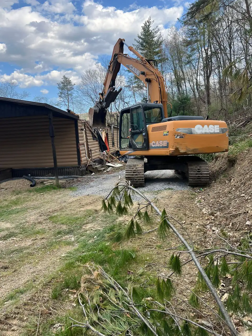 Orange tracked excavator with bucket near metal storage shed and wire fencing.