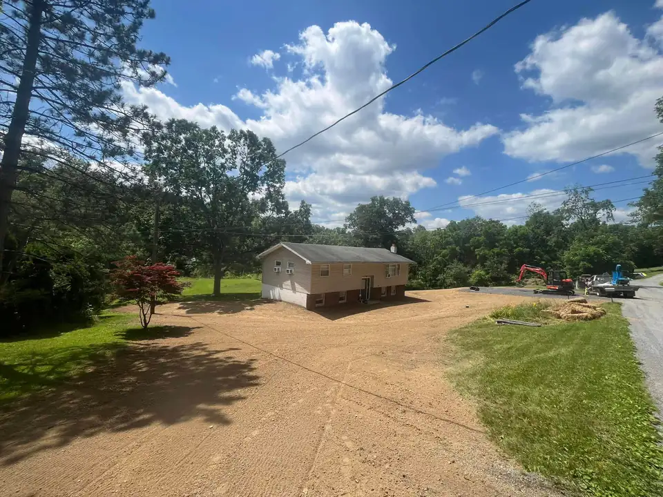 Gravel driveway leading to house with cleared yard and wooded trees in background.