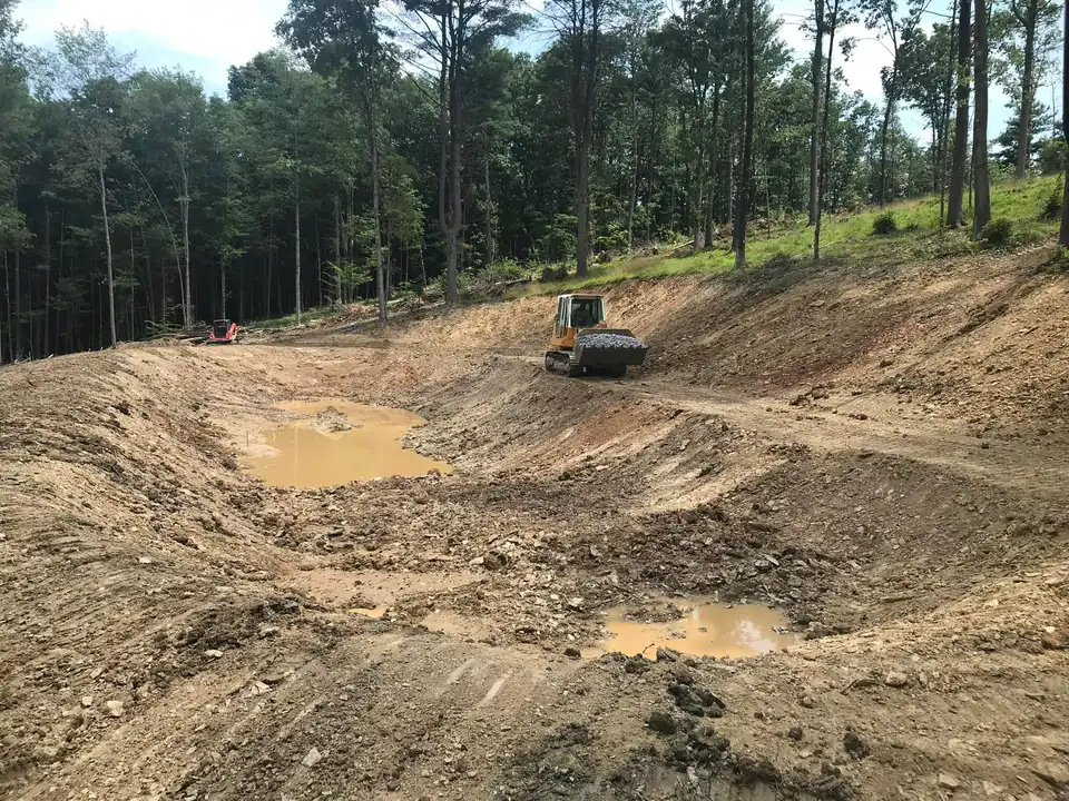 Tracked grading equipment on dirt lot surrounded by forest and exposed earth.