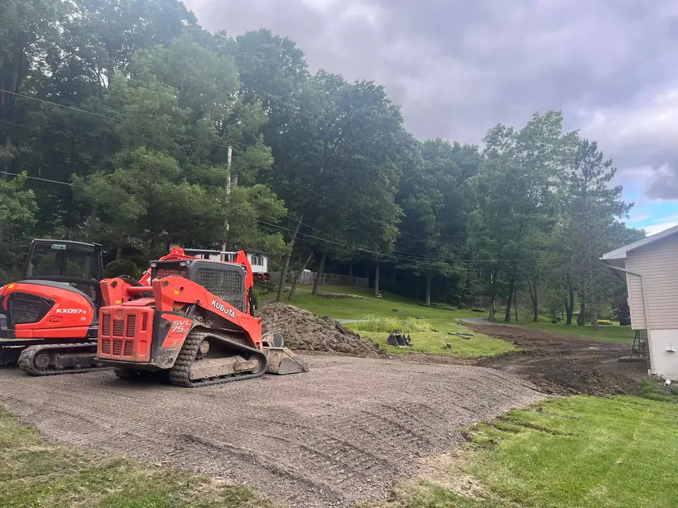 Red tracked machinery on cleared ground near house and landscaped trees.