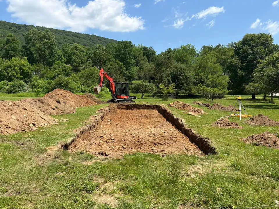 Red excavator in a field with excavated soil piles and trees in background