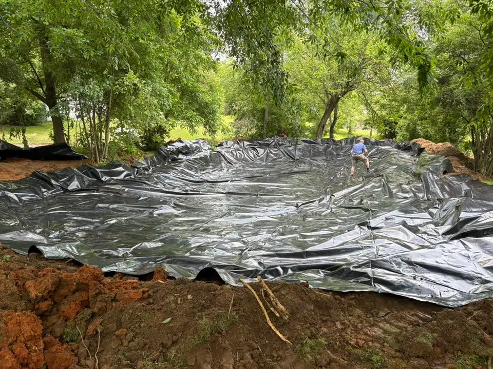 Black plastic sheeting laid over ground with trees surrounding