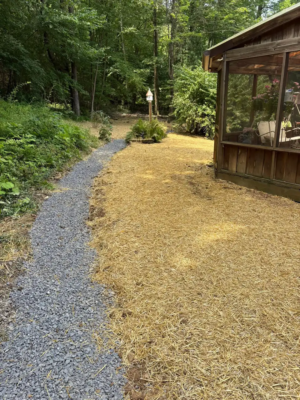 Gravel walkway with fresh straw beside a screened wooden porch