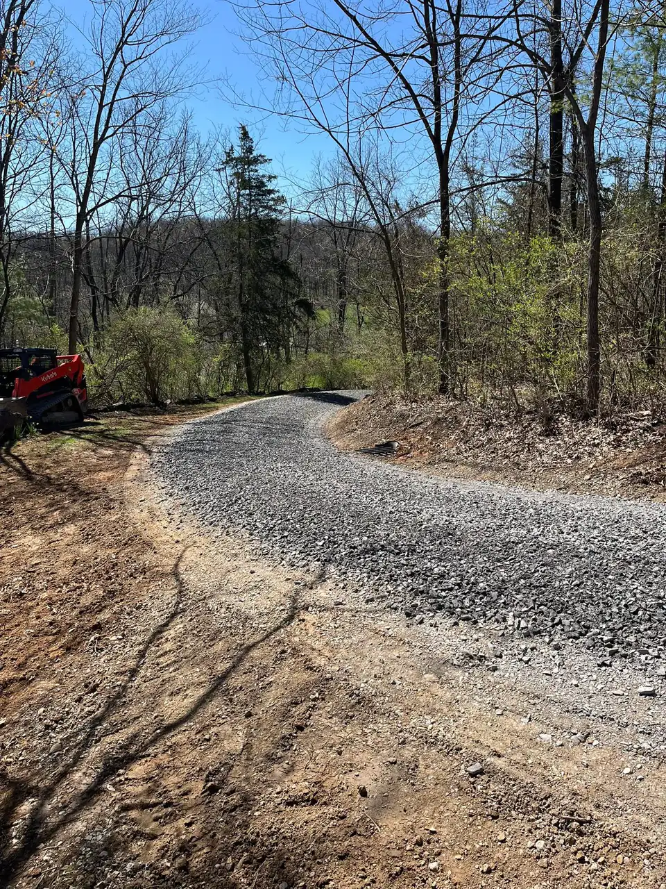 New gravel driveway curving down a wooded hillside
