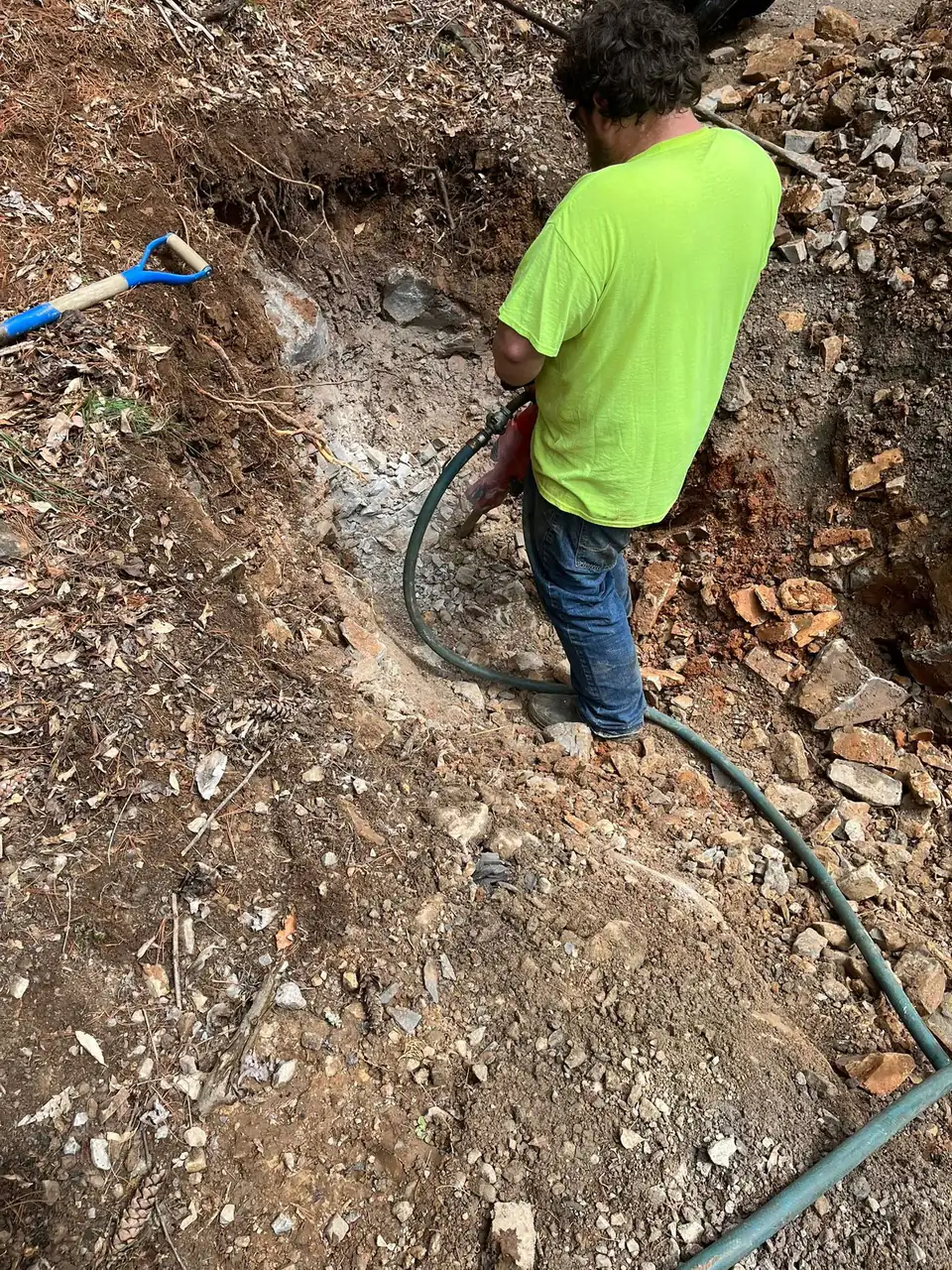 Crew member in a bright green shirt working with a hose in a rocky trench