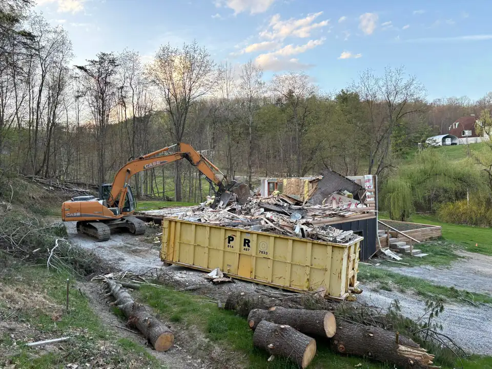 Orange excavator loading demolition debris into yellow metal container.