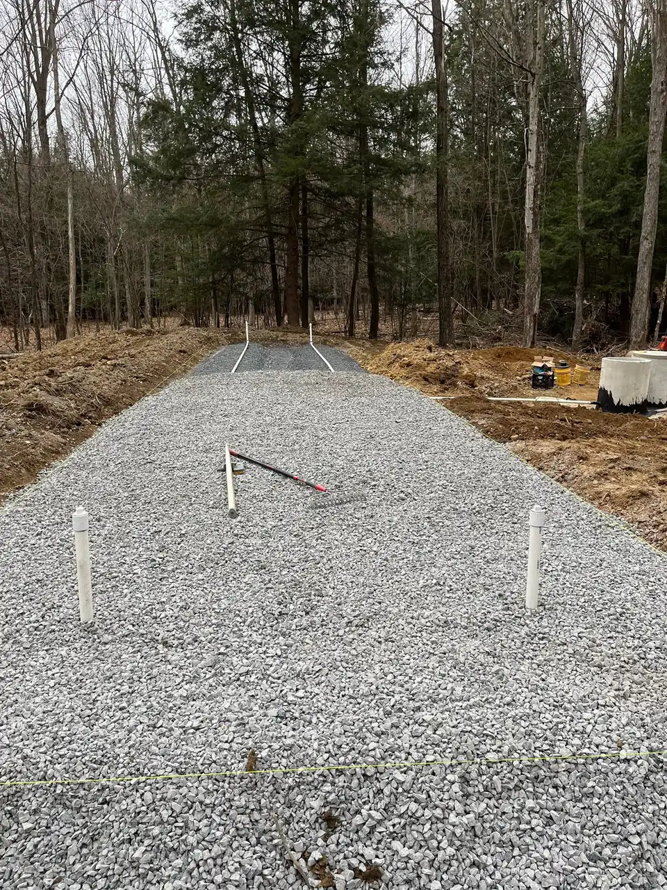 New gravel driveway in forest clearing with boundary markers and cleared earth.