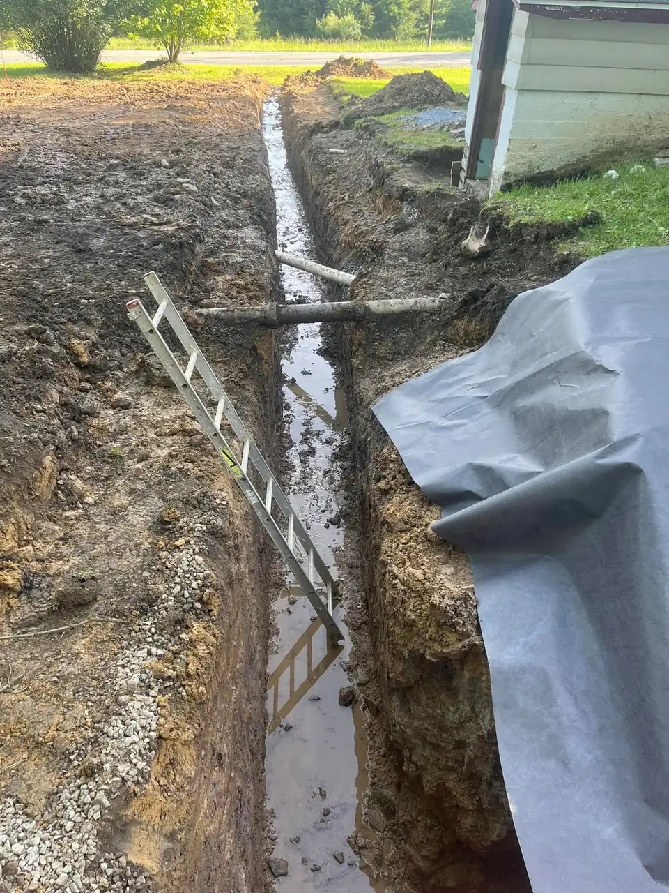 White pipe in wet trench with plastic protective sheeting and gravel base.