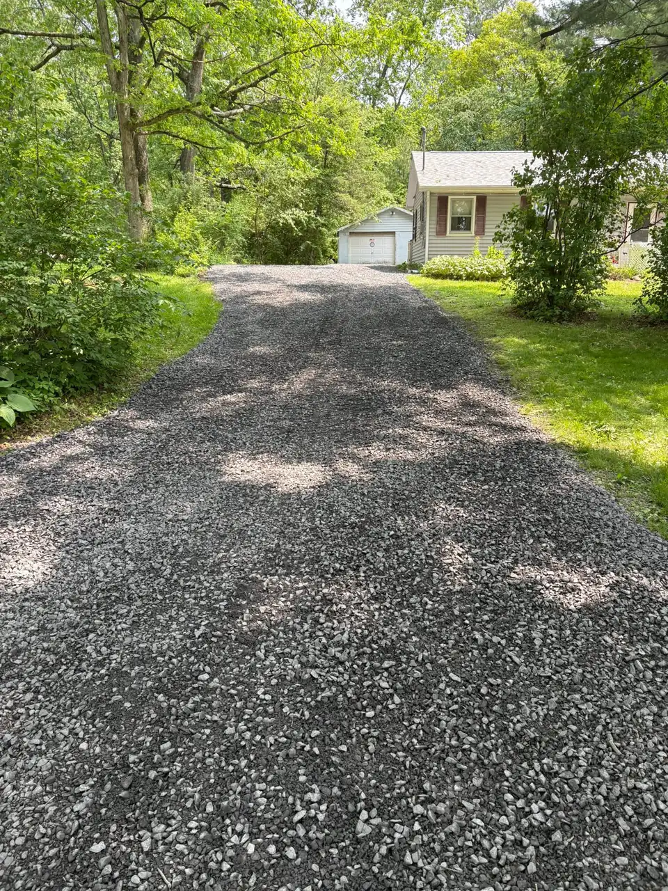 Gravel driveway leading to a small residential building surrounded by grass and dense vegetation