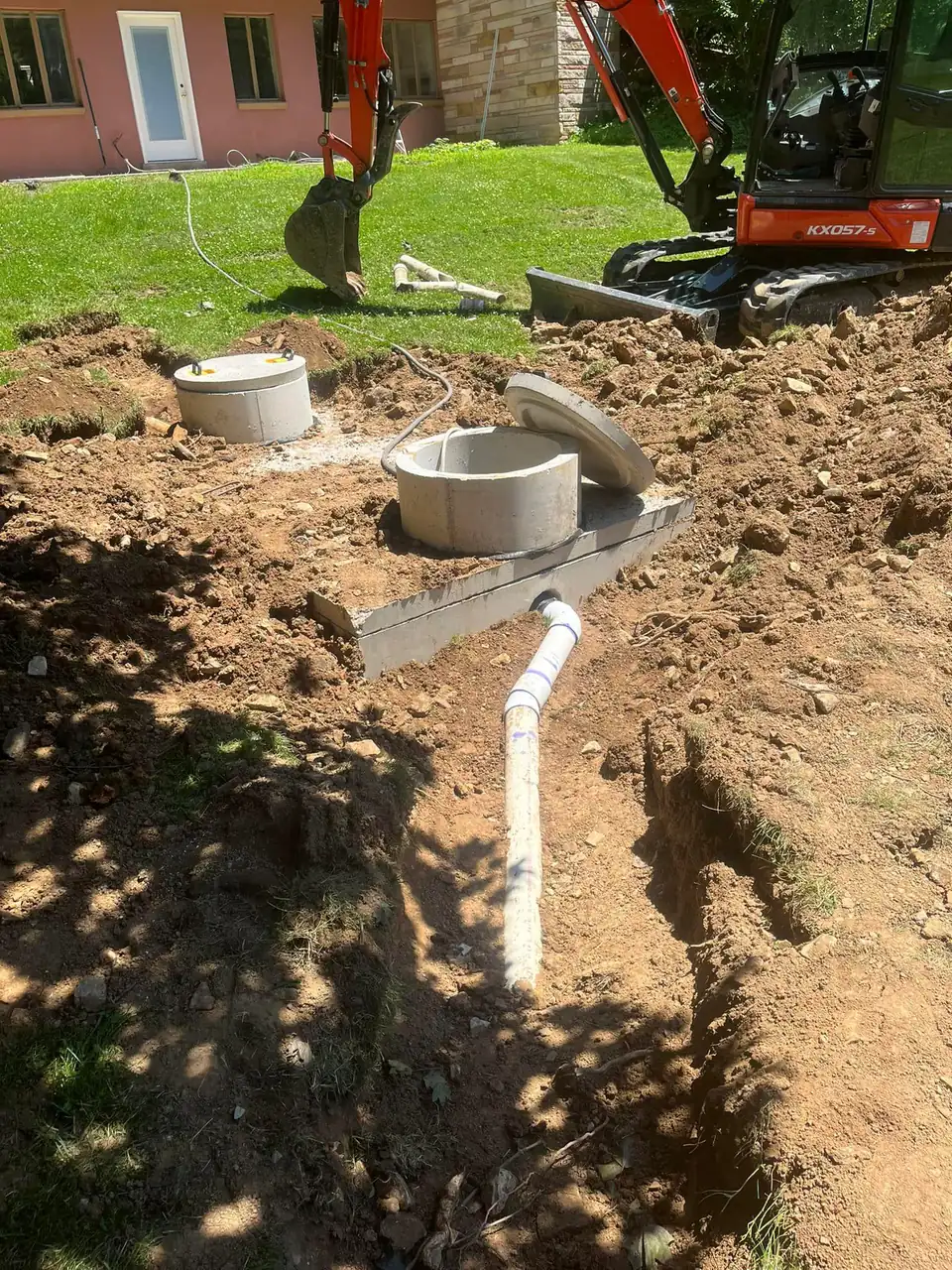 Excavated site showing concrete septic tanks, pipe, and house.