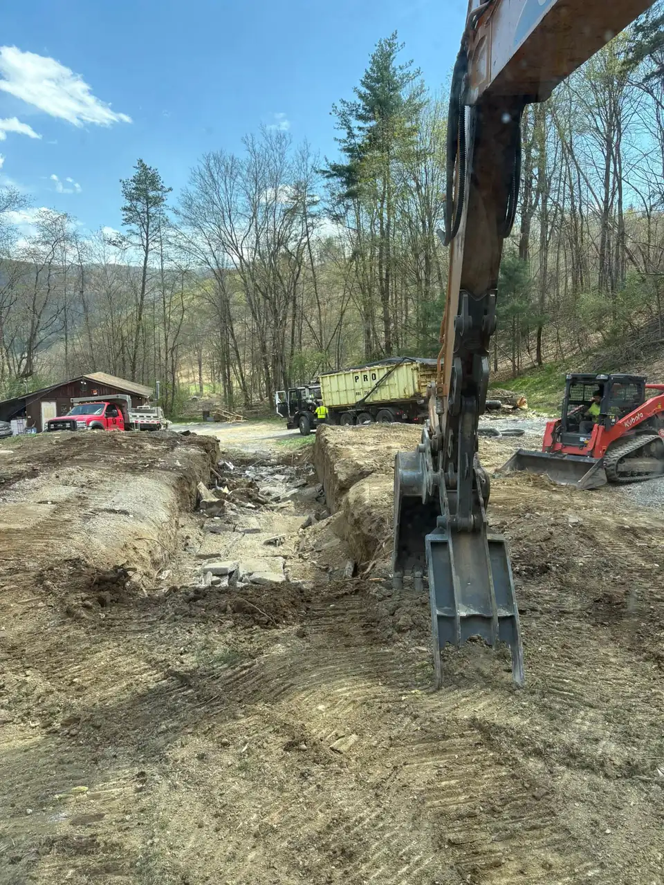 View from an excavator over a dug-out site with a tracked loader and buildings beyond