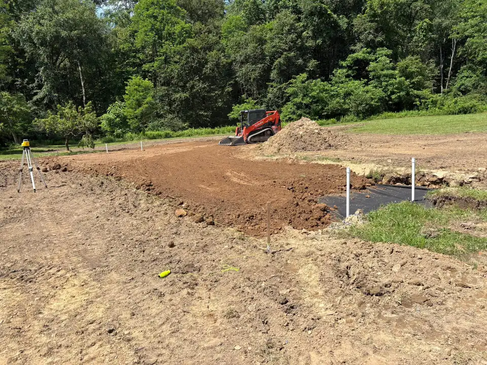 Skid steer grading dirt with marker stakes