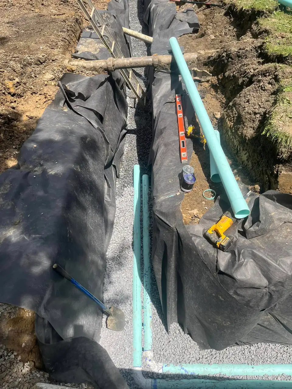 Fabric-lined trench with gravel and blue and green pipe