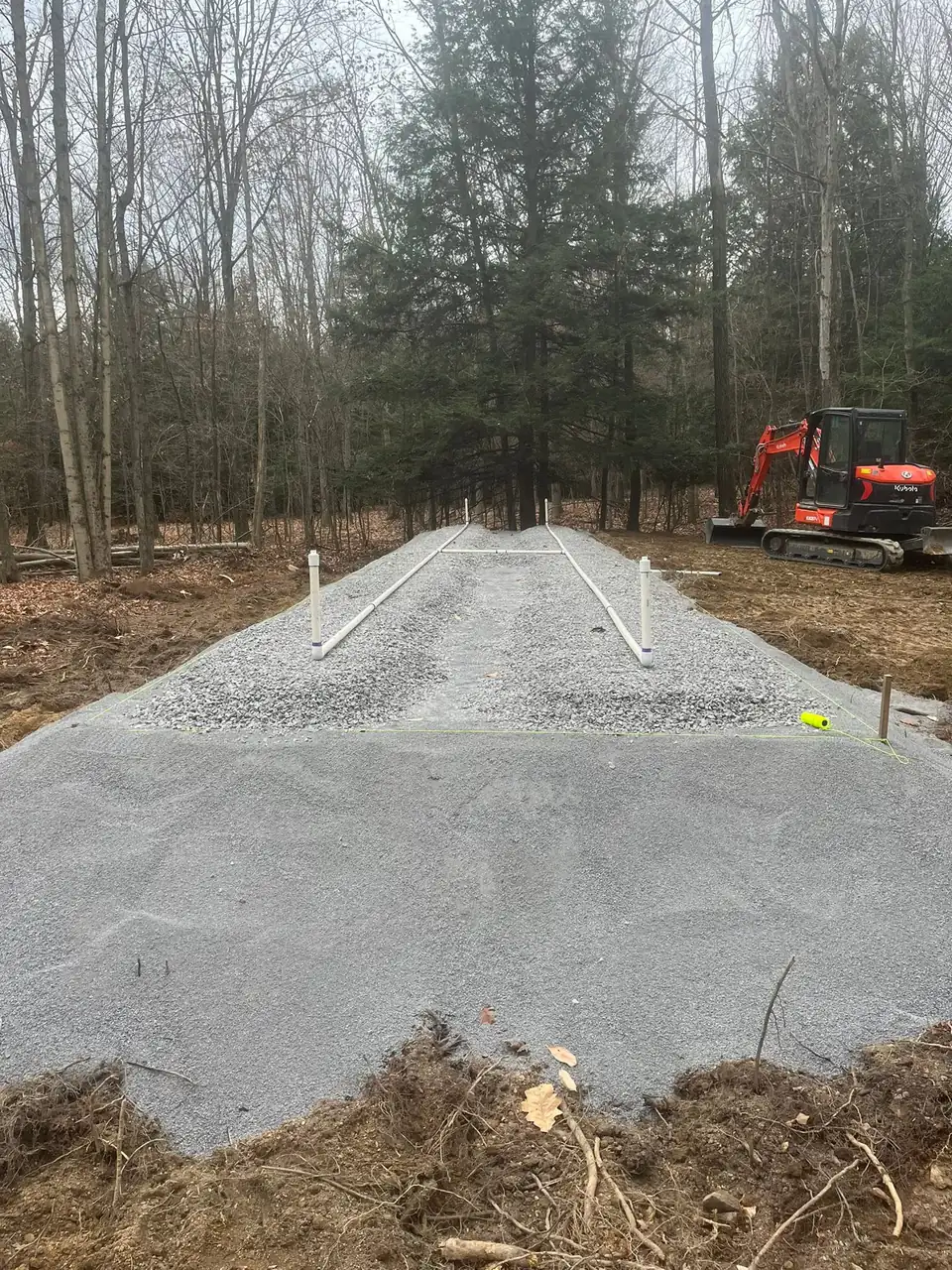 Gravel path through wooded land with equipment in background.
