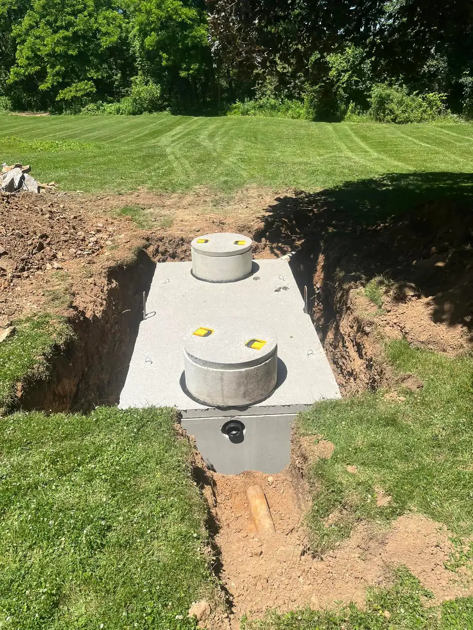 Multiple gray cylindrical tanks with metal covers in a dirt trench on grassy land.