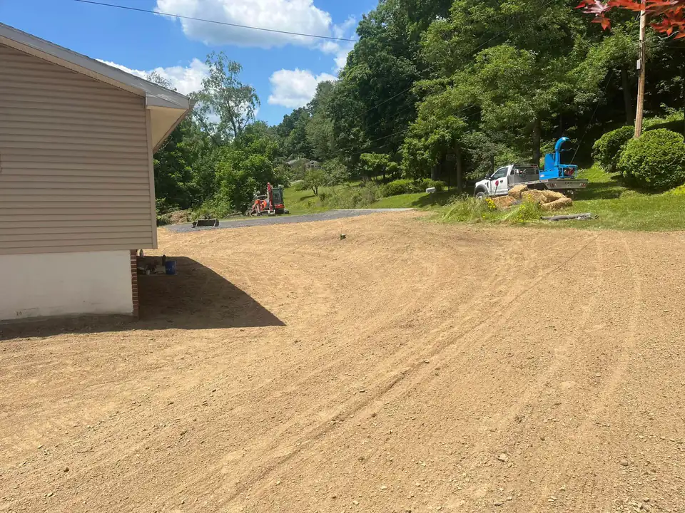 Freshly graded dirt yard beside a house with a truck and wood chipper beyond